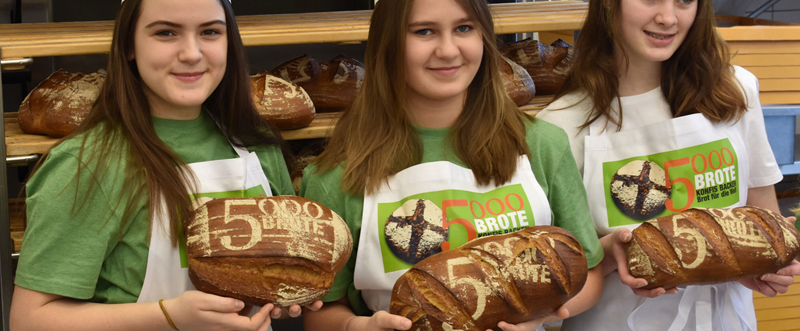 Drei Mädchen stehen in einer Backstube und halten Brot in den Händen