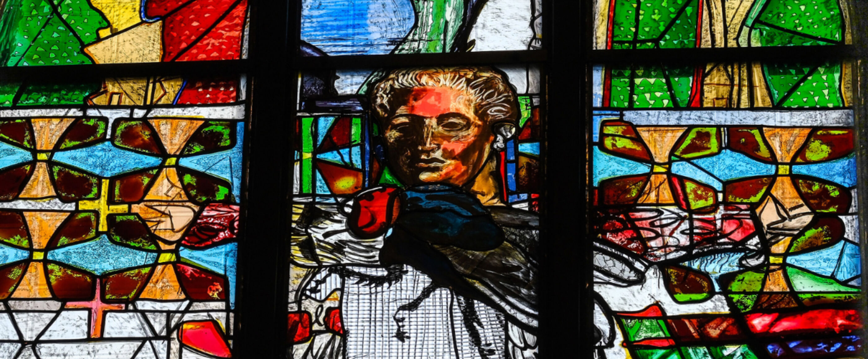 Ein buntes Kirchenfenster mit einem Bild von Martin Luther und einer großen Fliege ist zu sehen.