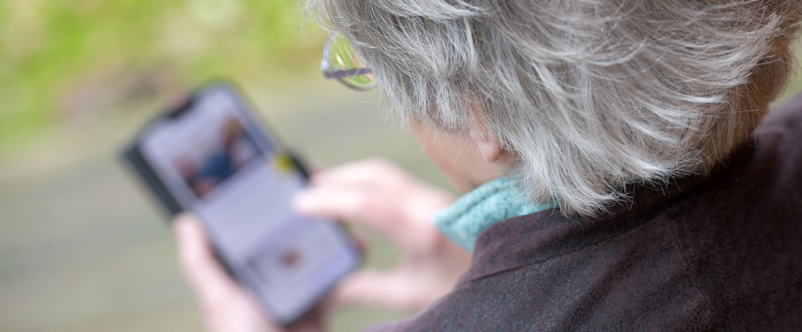 Eine ältere Frau mit grauen Haaren schaut auf ein Smartphone.