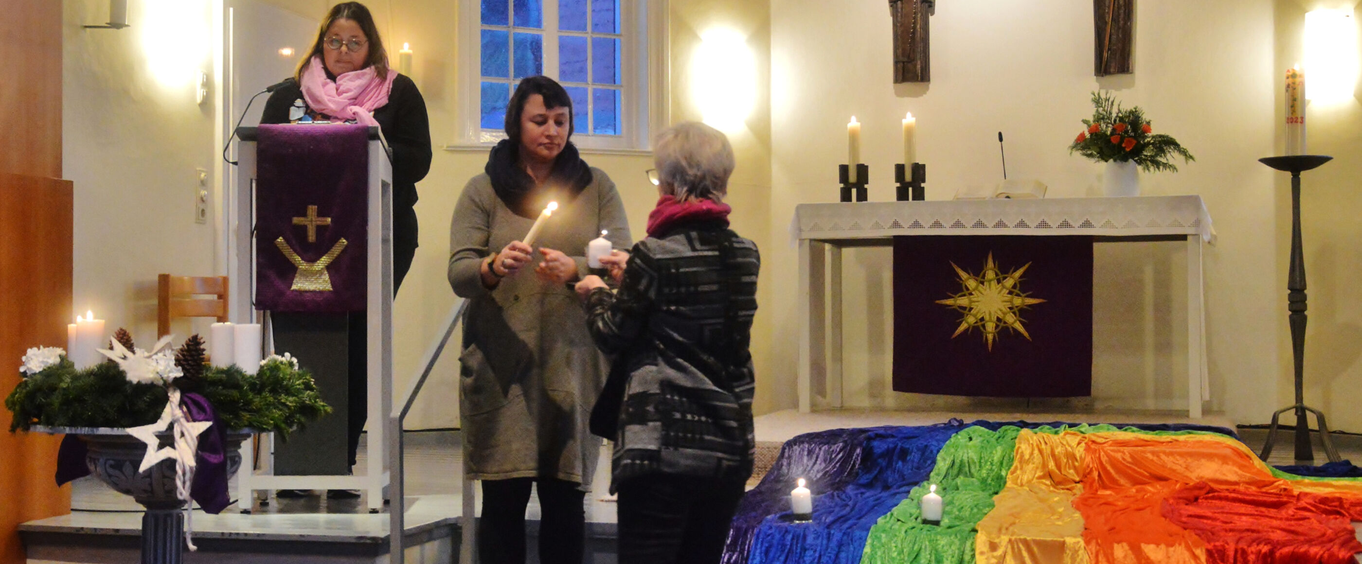 drei Frauen stehen bei einem Kirchenaltar und entzünden eine Kerze.