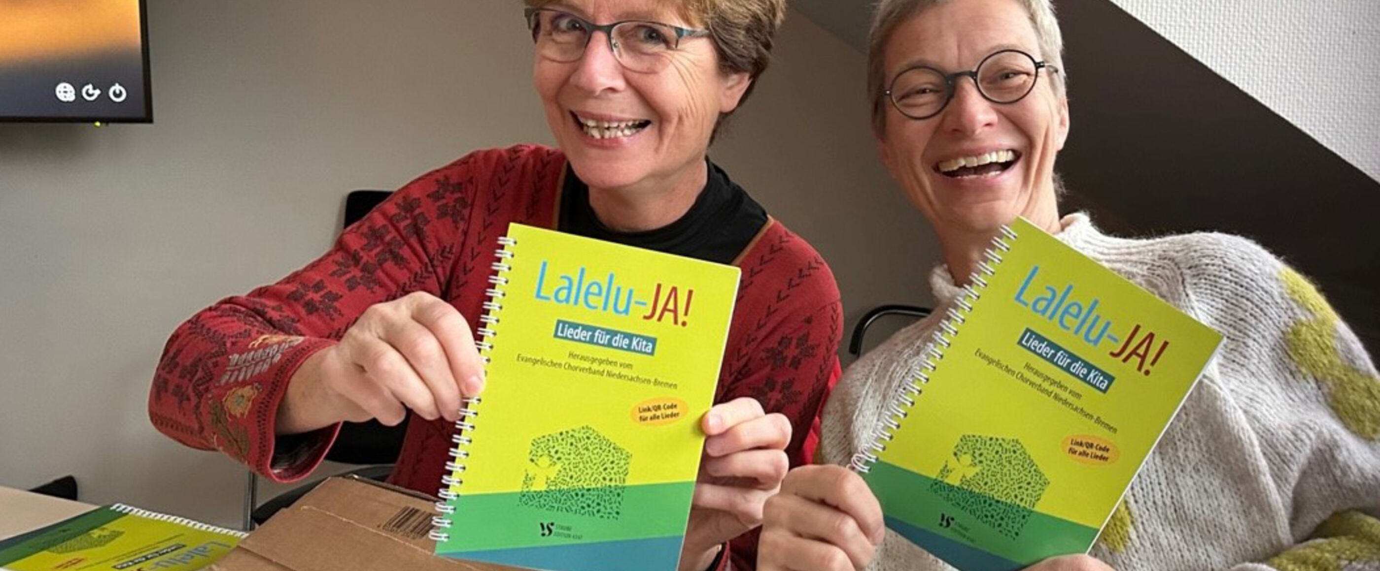 Zwei Frauen zeigen ein grünes Liederbuch mit dem Titel Lalelu-JA!