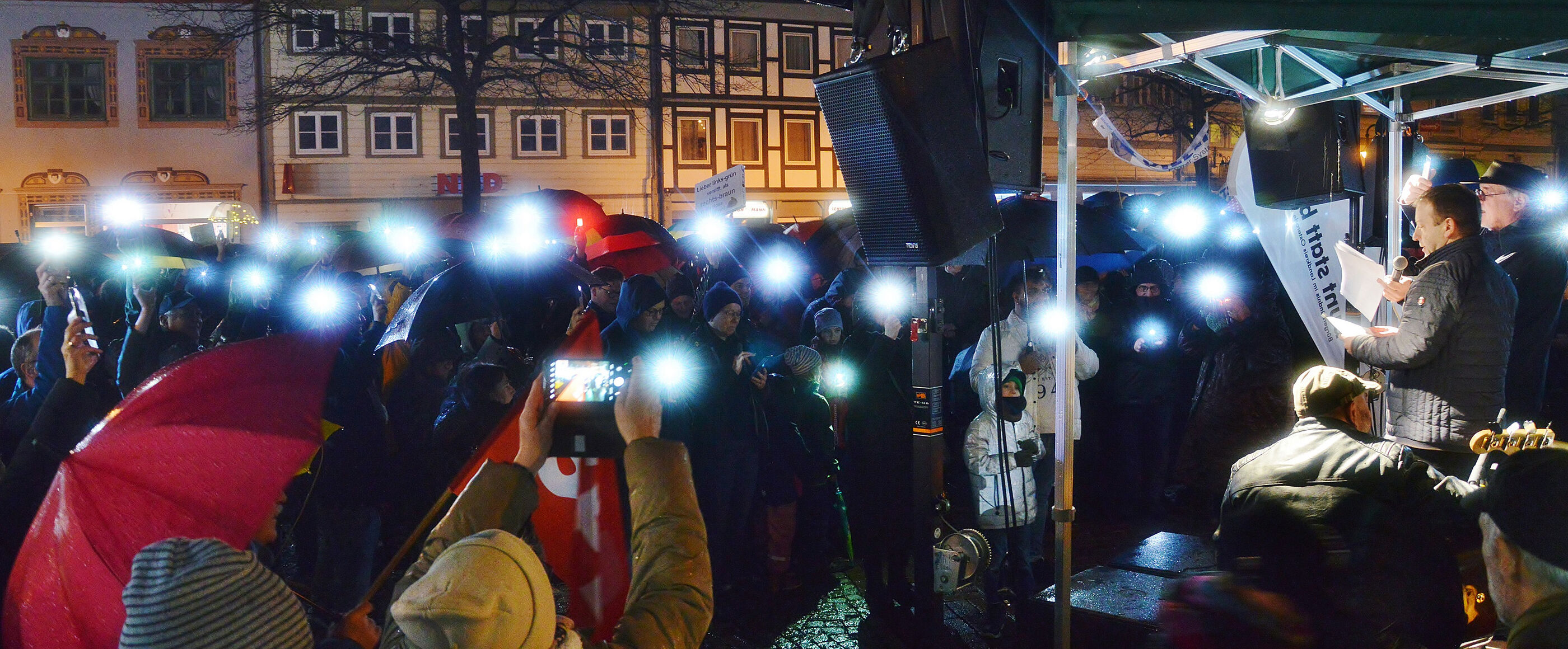 Eine Menschenmenge steht abends mit Lichtern vor einer Bühne.