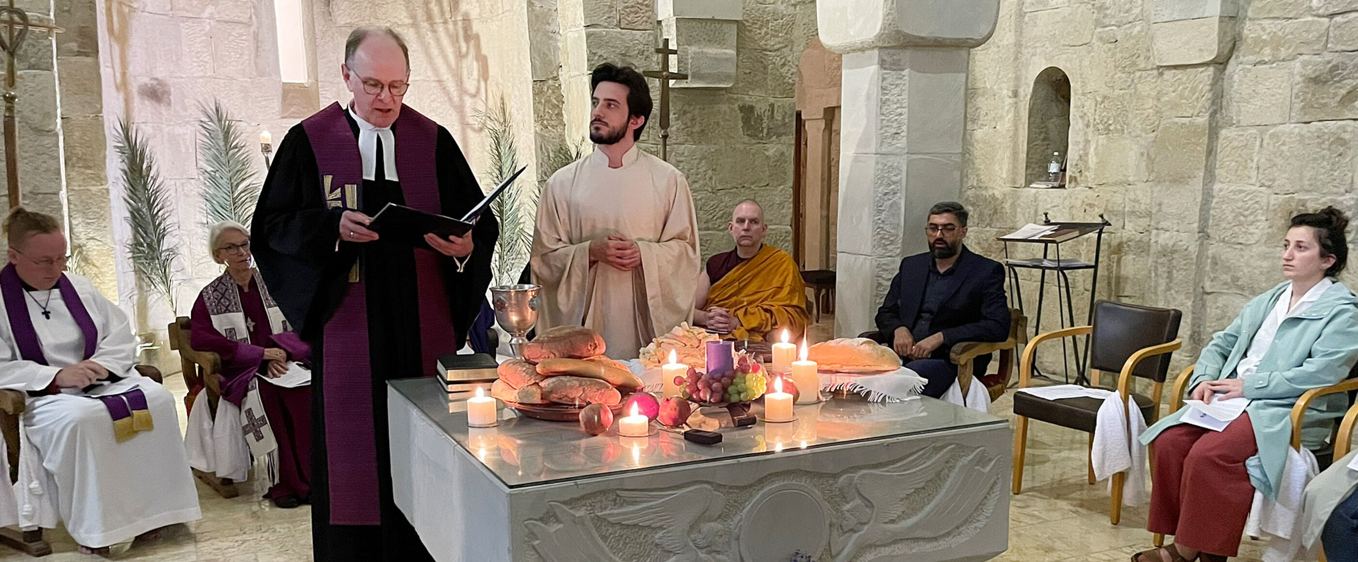 Ein Mann im Talar und ein Mann im weißen Gewand stehen hinter einem Altar, auf dem Kerzen, Brote und ein Kelch stehen.