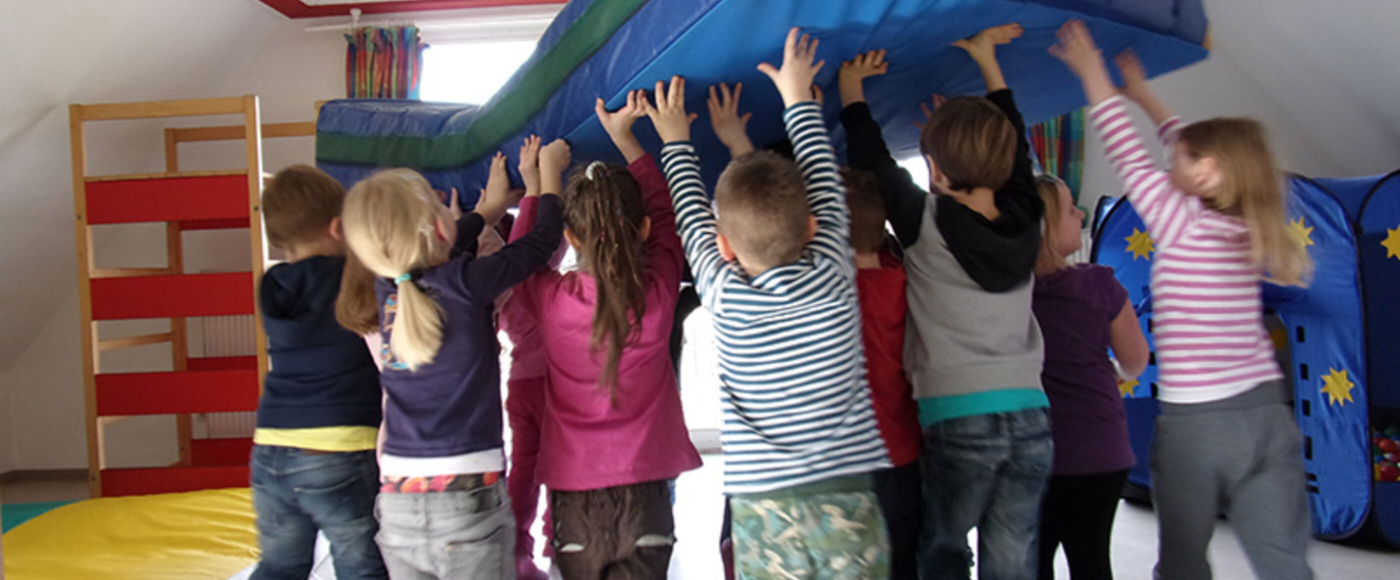 Mehrere Kinder stemmen gemeinsam eine Matratze in die Höhe.
