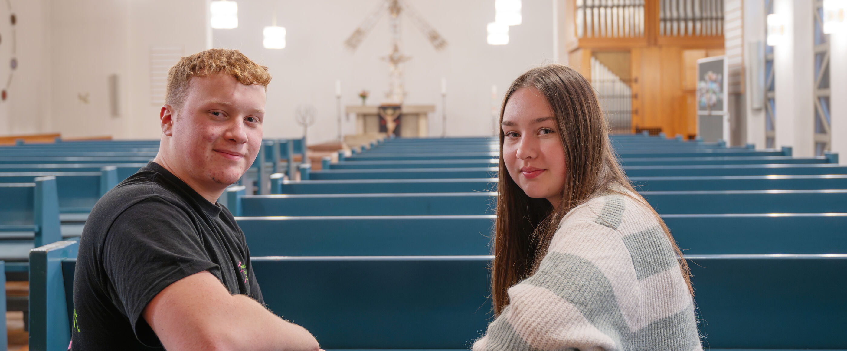 Ein junger Mann und eine junge Frau sitzen in einer Kirche auf einer Kirchenbank.