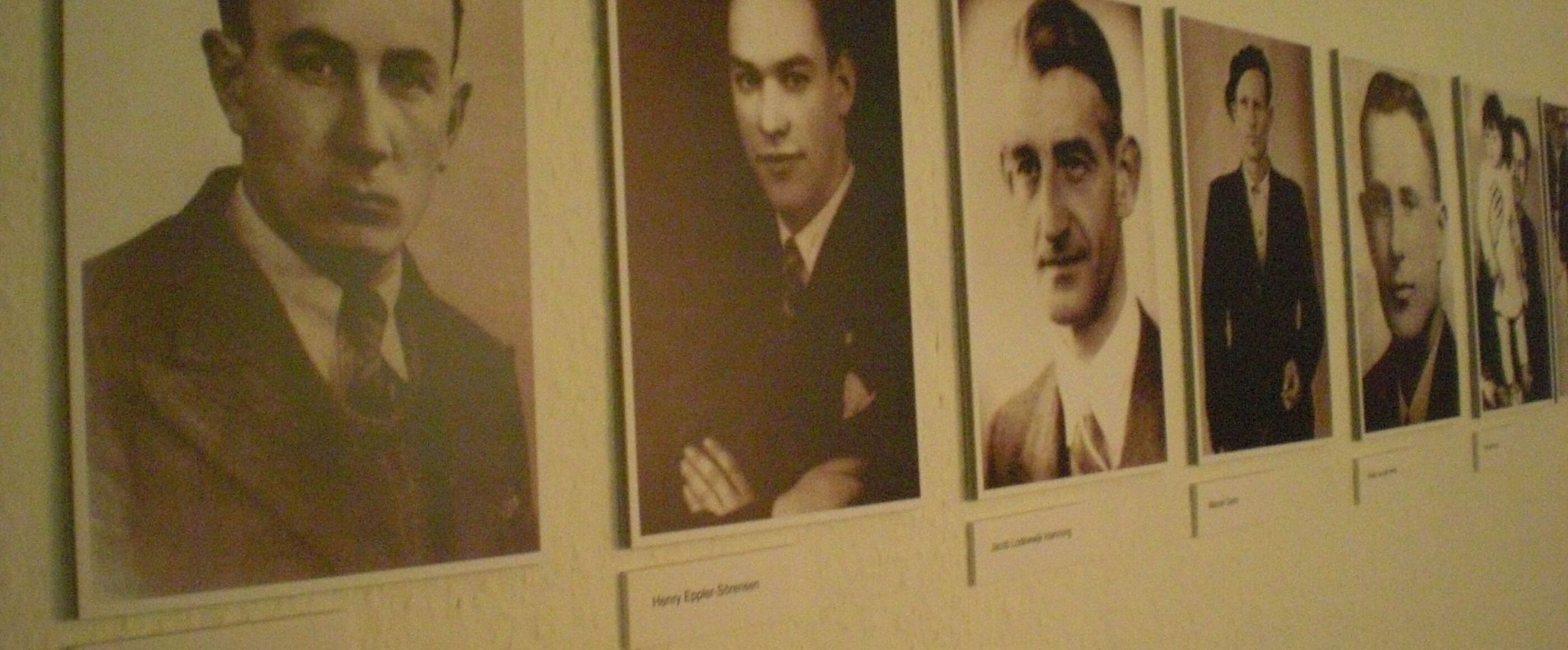 Mehrere schwarz-weiß Bilder von jungen Männern hängen an einer Wand.