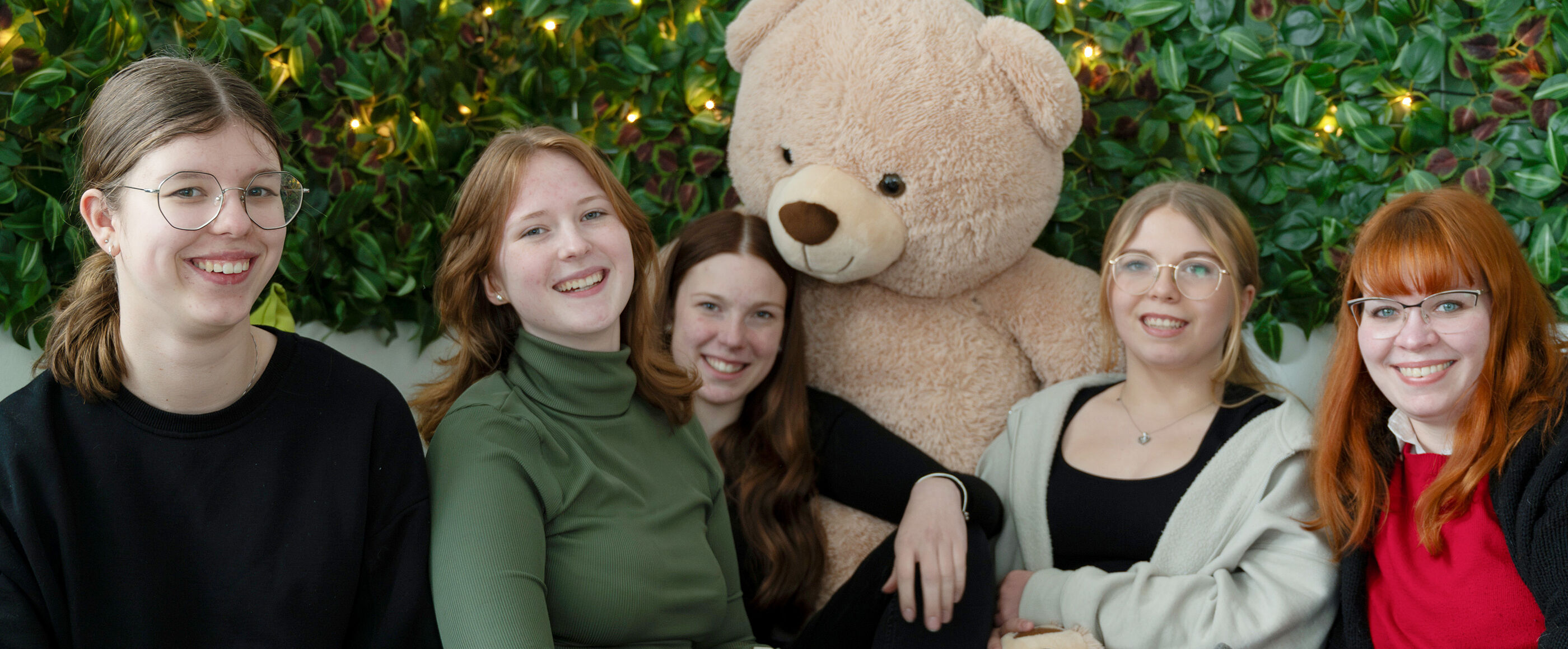 Fünf als Mädchen lesbare Personen sitzen mit einem Teddy in der Sofa-Ecke eines Jugendtreffs.