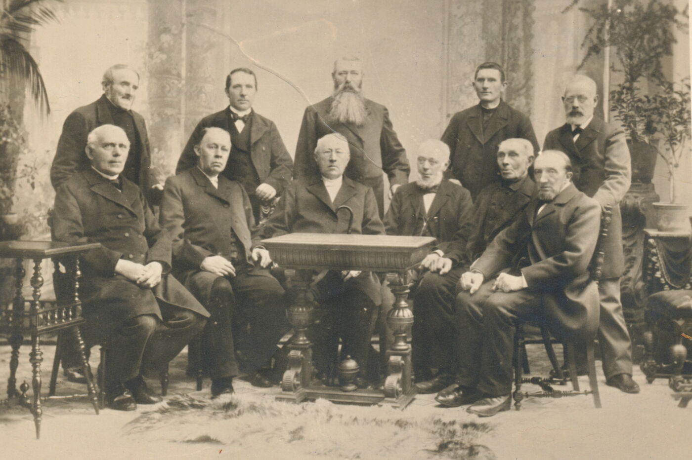 Das Bild zeigt eine historische Aufnahme von zehn männlich lesbaren Personen, die sich in zwei Reihen hinter einem Tisch postiert haben für das Foto; sie tragen dunkle Anzüge.