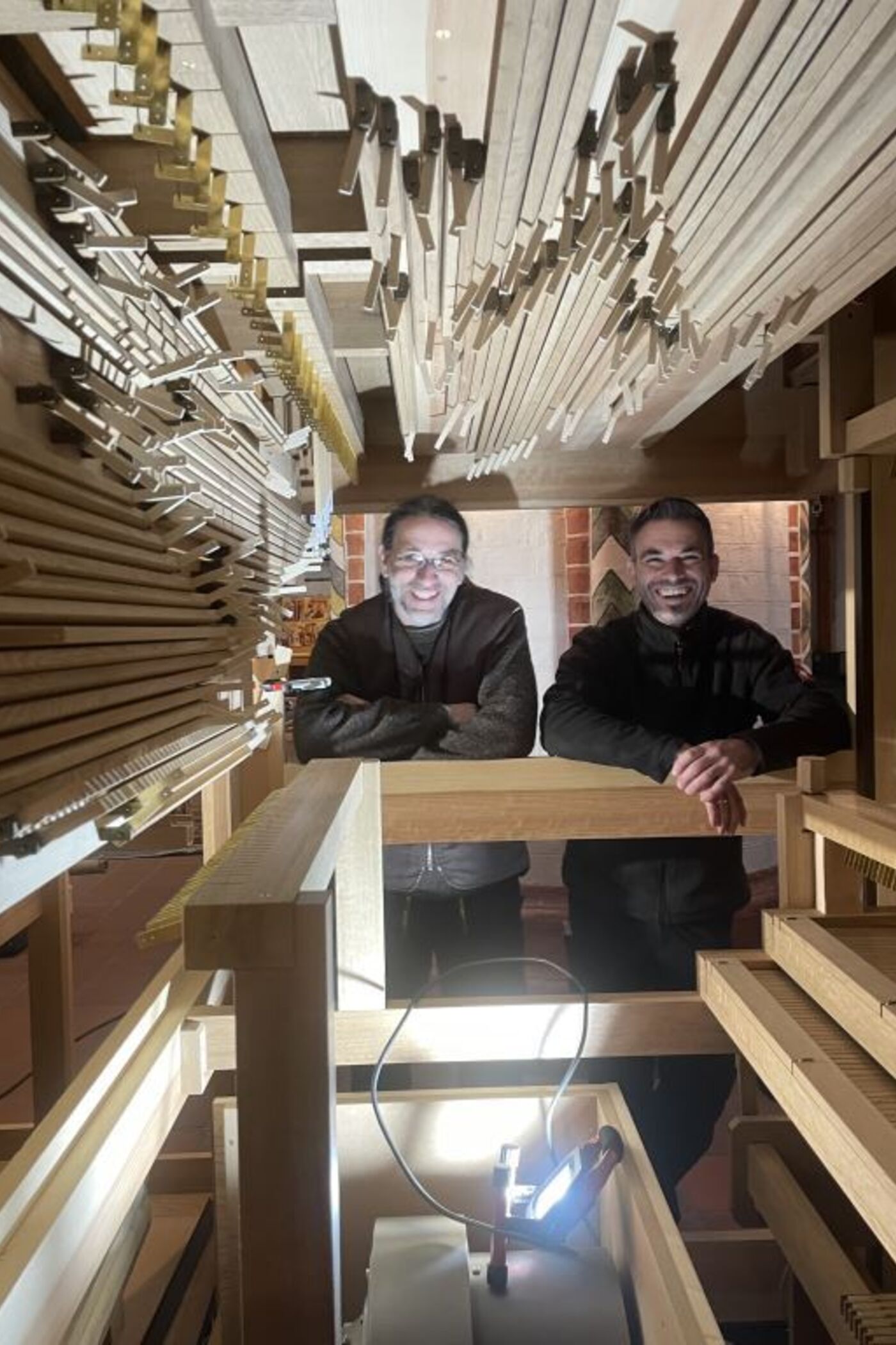 Zwei als Männer lesbare Personen blicken aus dem Inneren einer Orgel.