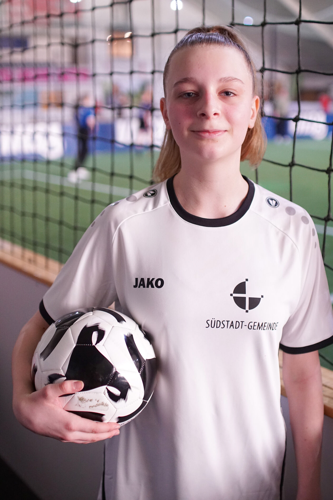 Ein Mädchen mit weißem Trikot und Fußball unter dem Arm.