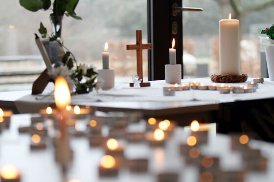Das Bild zeigt zwei Tische vor einem Fenster, die mit Kerzen und einem christlichen Kreuz geschmückt sind.