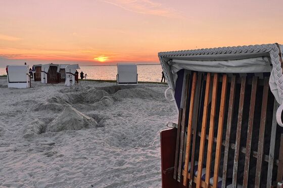 Ein Strandkorb bei Sonnenuntergang. Im Hintergrund sieht man das Meer.