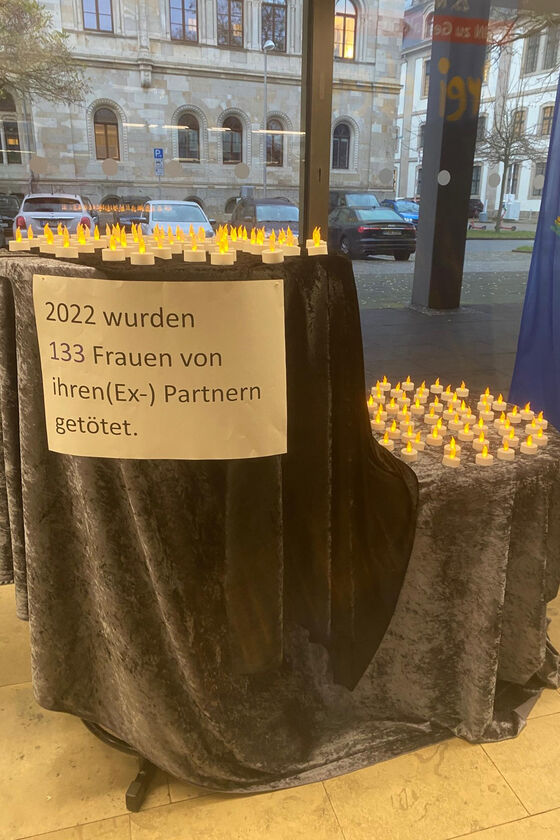 Teelichter stehen auf zwei mit Samtdecken gedeckten Tischen. Auf einem Schild steht: 2022 wurden 133 Frauen von ihren (Ex-)Partnern getötet.
