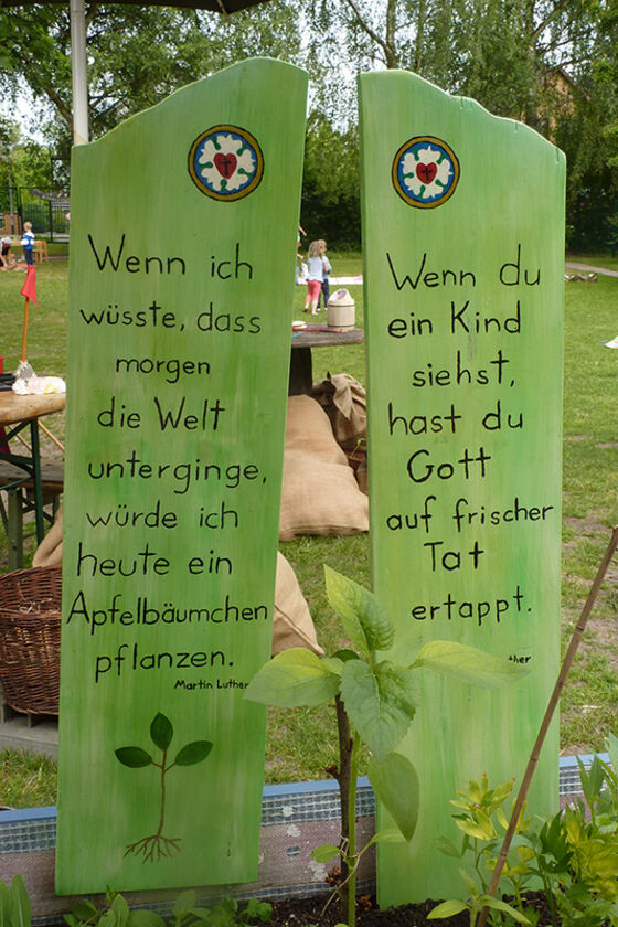 Auf zwei grünen Tafeln steht: "Wenn ich wüsste, das morgen die Welt unterginge, würde ich heute noch ein Apfelbäumchen pflanzen. Martin Luther." Und: "Wenn Du ein Kind siehst, hast Du Gott auf frischer Tat ertappt."