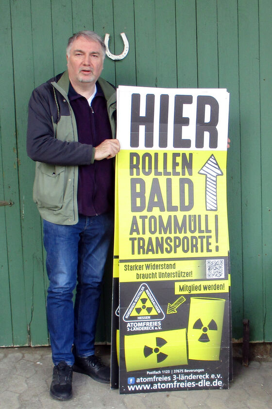 Ein Mann steht vor einem Scheunentor und hält ein Plakat mit der Aufschrift "Hier rollen bald Atommüll-Transporte!"