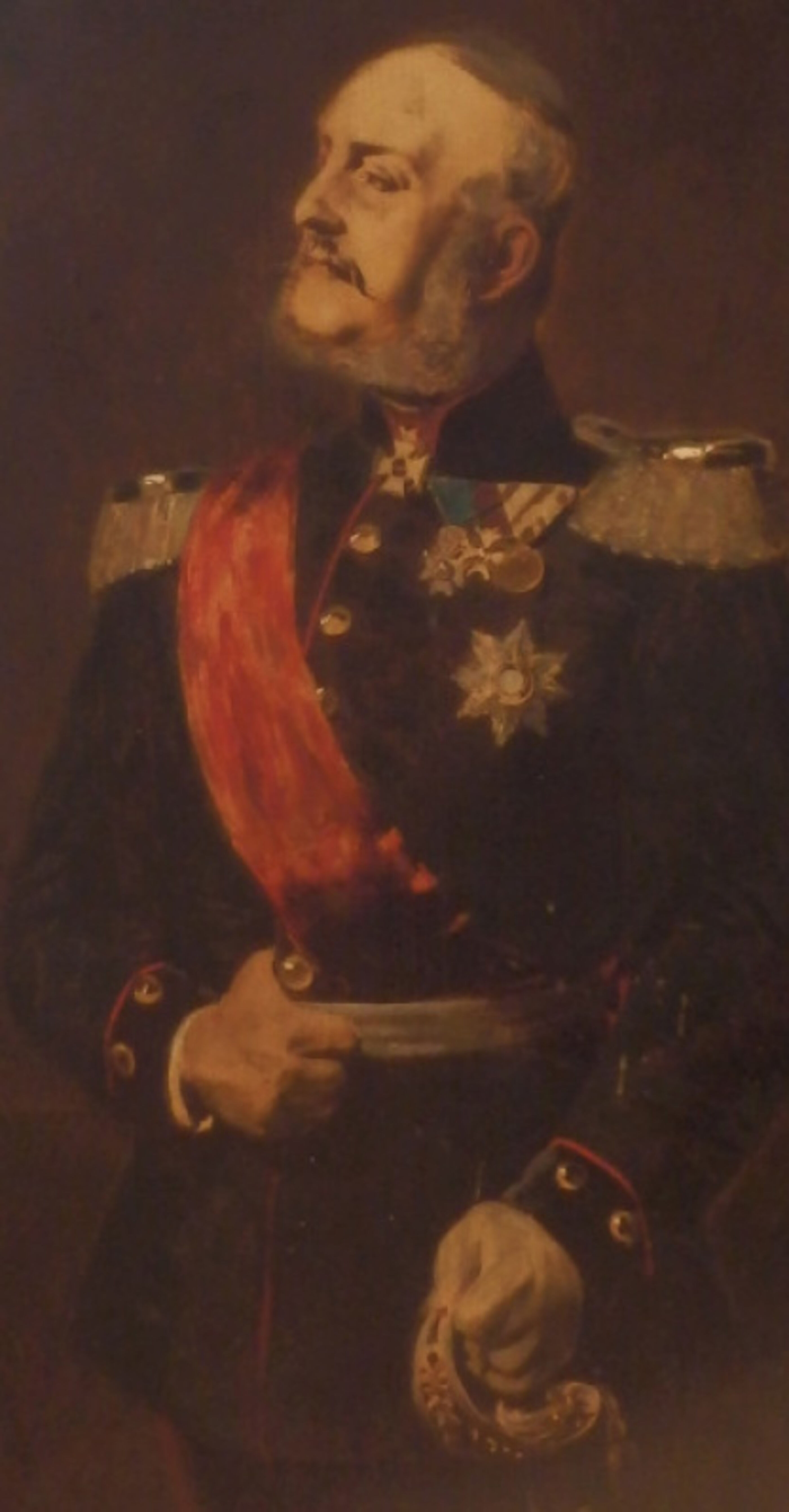 Das Bild zeigt ein Ölgemälde von König Georg V., eine männlich lesbare Person in Uniform mit kurzen grauen Haaren, einem Schnurbart, mit Schärpe und Orden.