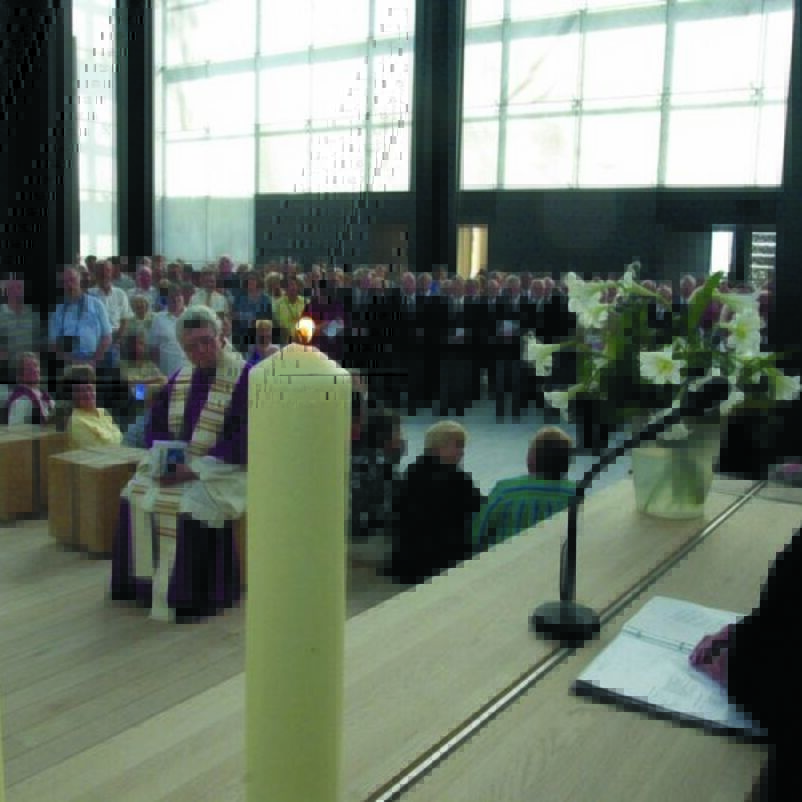 Das Bild zeigt eine weiblich lesbare Person, die in einem hellen modernen Gebäude am Altar steht und mit vielen Menschen Gottesdienst feiert.