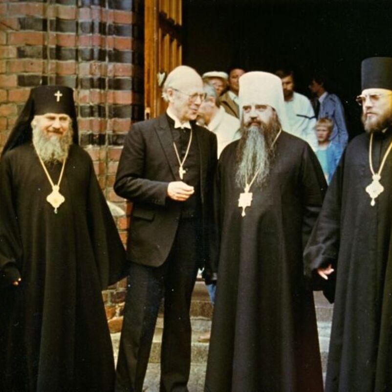 Das Bild zeigt einen Gruppe von männlich lesbaren Personen, einige davon in kirchlichen Gewändern, vor dem Eingang einer Kirche.