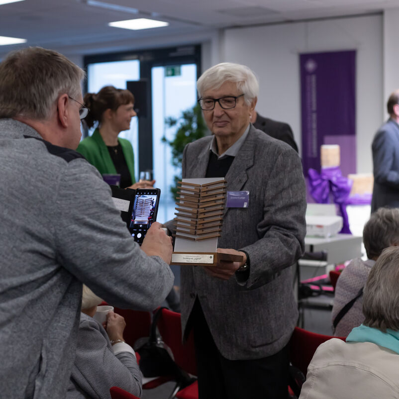 Ein männlich zu lesender Preisträger hält seinen Pokal für ein Foto in die Kamera.