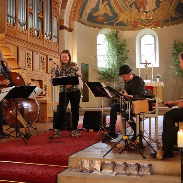 Das Bild zeigt eine Kirche von innen mit vier Menschen, die im Altarraum Musik machen. 