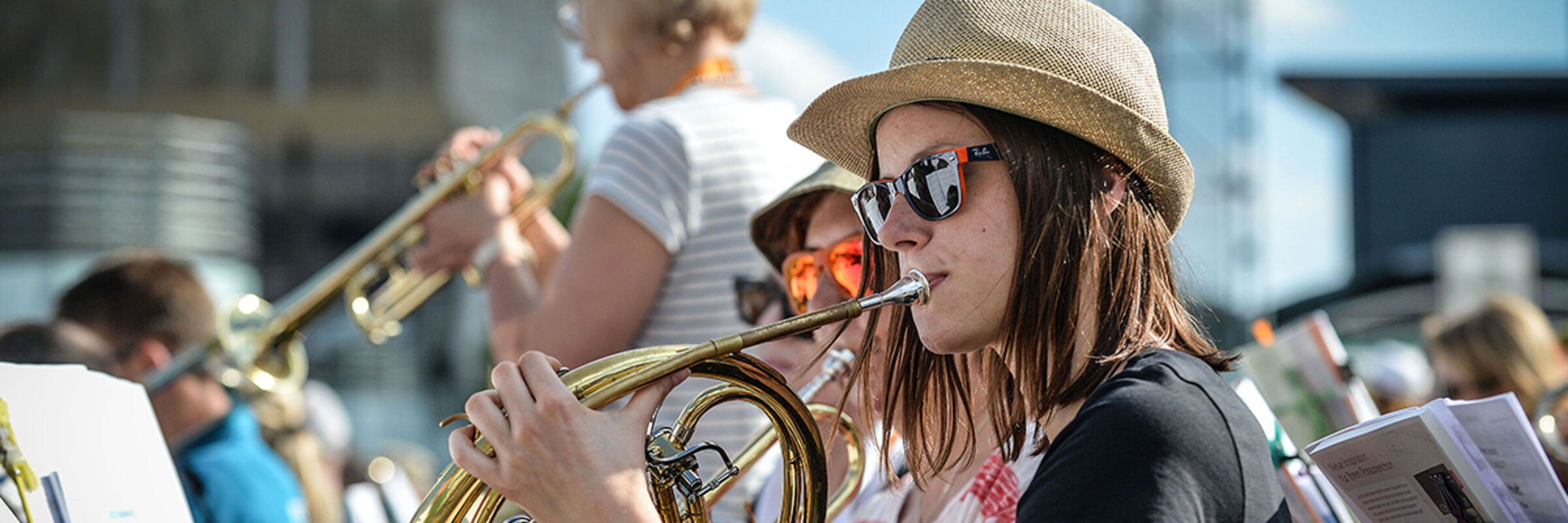Eine junge Frau mit Sonnenbrille spielt Horn